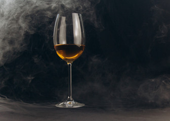 a glass of white wine on a black background. the smoke from the hookah envelops the glass. rest, holiday. alcoholic drink closeup. white fog