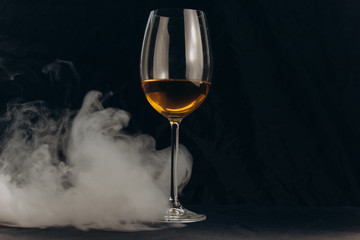 a glass of white wine on a black background. the smoke from the hookah envelops the glass. rest, holiday. alcoholic drink closeup. white fog