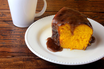 slice of carrot cake with chocolate coating on white ceramic plate on rustic wooden table