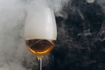 a glass of white wine on a black background. the smoke from the hookah envelops the glass. rest, holiday. alcoholic drink closeup. white fog in a glass. fog