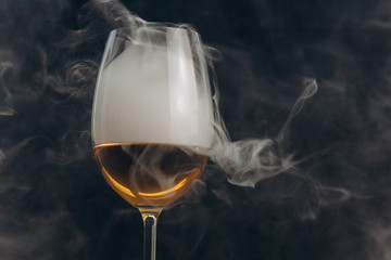 a glass of white wine on a black background. the smoke from the hookah envelops the glass. rest, holiday. alcoholic drink closeup. white fog in a glass. fog