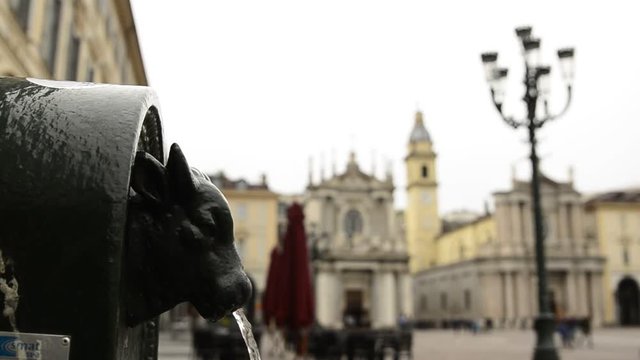 Turin, Piedmont, Italy. April 2019. A look at Piazza San Carlo. On the left in the foreground the fountain with the green bull, called turet, on the right the two twin churches. People are walking.