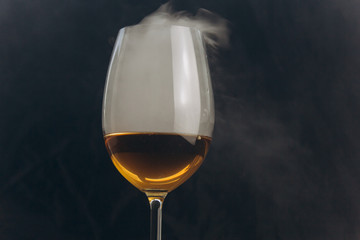 a glass of white wine on a black background. the smoke from the hookah envelops the glass. rest, holiday. alcoholic drink closeup. white fog in a glass. fog