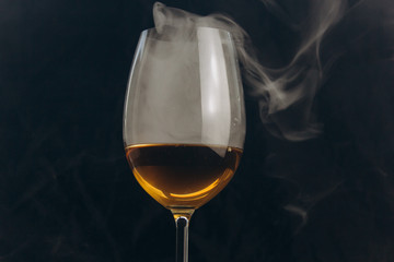a glass of white wine on a black background. the smoke from the hookah envelops the glass. rest, holiday. alcoholic drink closeup. white fog in a glass. fog