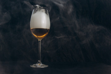 a glass of white wine on a black background. the smoke from the hookah envelops the glass. rest, holiday. alcoholic drink closeup. white fog in a glass. fog