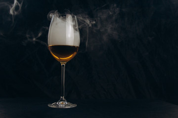 Obraz na płótnie Canvas a glass of white wine on a black background. the smoke from the hookah envelops the glass. rest, holiday. alcoholic drink closeup. white fog in a glass. fog