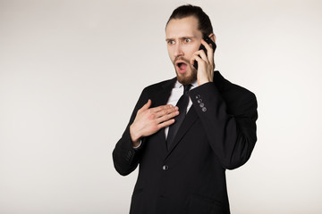 Waist up portrait of bearded young businessman in black suit surprised by the heard news from a business partner