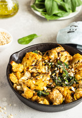 Roasted cauliflower with spinach, raisin and nuts in a cast-iron pan. Light grey background. Copy space. Healthy vegan food.