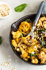 Roasted cauliflower with spinach, raisin and nuts in a cast-iron pan. Light grey background. Copy space. Healthy vegan food.