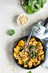 Roasted cauliflower with spinach, raisin and nuts in a cast-iron pan. Light grey background. Copy...