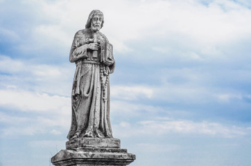 Obraz premium Ancient religious statue in the old cemetery on the background sky with clouds. Jesus with bible