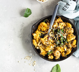 Roasted cauliflower with spinach, raisin and nuts in a cast-iron pan. Light grey background. Copy...