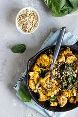 Roasted cauliflower with spinach, raisin and nuts in a cast-iron pan. Light grey background. Copy space. Healthy vegan food.