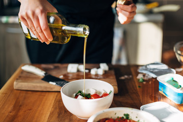 Female chef pouring olive oil on a greek salad