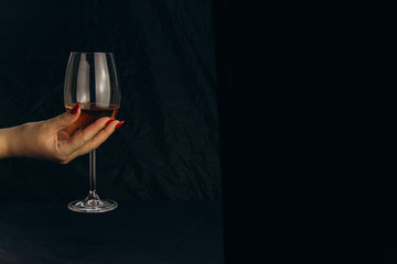 Fototapeta na wymiar cropped female hand holding a glass of white wine on a black background. rest, holiday, party. isolated alcoholic drink closeup.