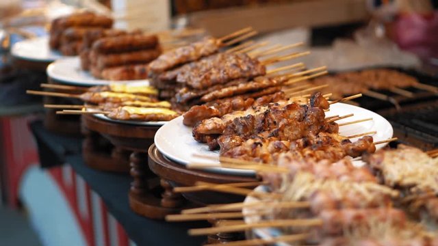 A lot of portions of fried meat kebabs are on white plates on the counter. Fresh BBQ skewers closeup, slow motion