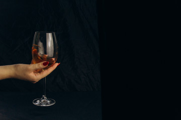 Naklejka na ściany i meble cropped female hand holding a glass of white wine on a black background. rest, holiday, party. isolated alcoholic drink closeup.