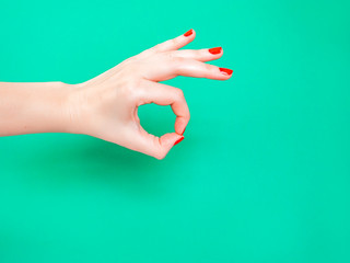 Woman hand holding something with two fingers on isolated turquoise green color background.