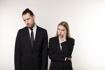 Two business partners in black suits, handsome bearded man and beautiful blonde woman shocked don't know what to do