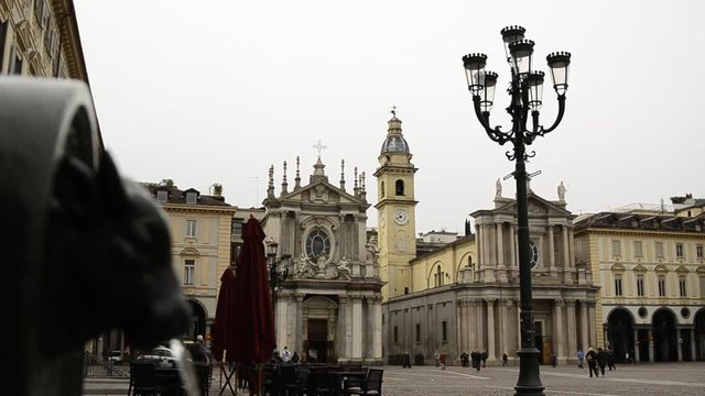 Turin, Piedmont, Italy. April 2019. A look at Piazza San Carlo. On the left in the foreground the fountain with the green bull, called turet, on the right the two twin churches. People are walking.