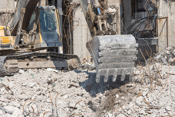 Metal bucket hydraulic excavator boom digs stones and debris of a demolished building. Close up view.