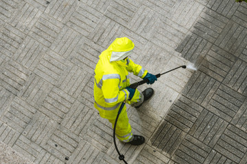 Top view of a Worker cleaning the street sidewalk with high pressure water jet on rainy day