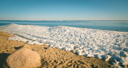 Snow pile on the beach, hill. Large snow drift isolated on a blue sky background,  outdoor view of ice blocks at frozen finland lake in winter