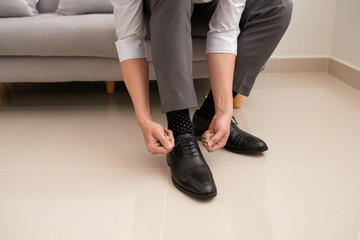 Man's hands tying shoelace of his new shoes. People, business, fashion and footwear concept - close up of man leg and hands tying shoe laces.