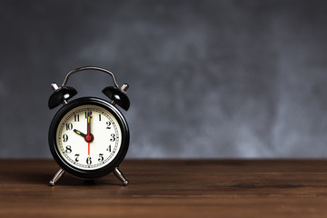Vintage / retro black analog alarm clock on wooden table with copy space on dark background. Clock...