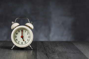 Clock hand at 5 o'clock alarm at 5 o'clock. Vintage / retro white analog alarm clock on wooden...