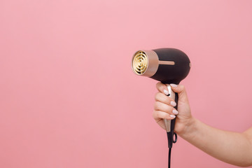 in hand of woman hair dryer on pink background