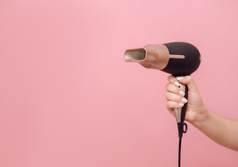 in hand of woman hair dryer on pink background