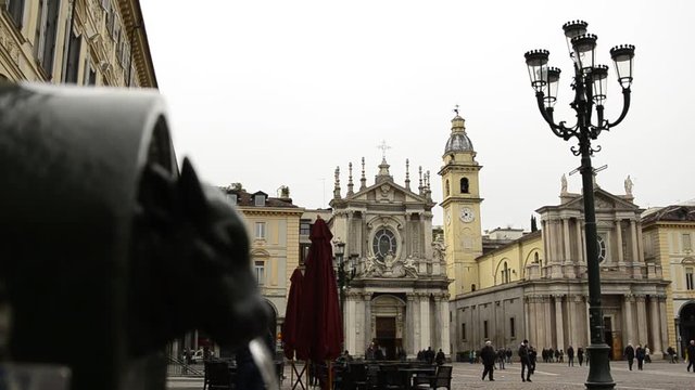 Turin, Piedmont, Italy. April 2019. A look at Piazza San Carlo. On the left in the foreground the fountain with the green bull, called turet, on the right the two twin churches. People are walking.