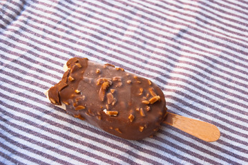 Frozen chocolate ice cream on stick on striped background.