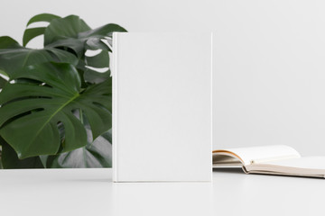 White book mockup with workspace accessories and a monstera plant.