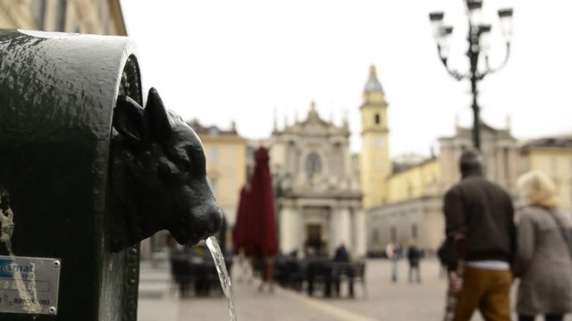 Turin, Piedmont, Italy. April 2019. A look at Piazza San Carlo. On the left in the foreground the fountain with the green bull, called turet, on the right the two twin churches. People are walking.