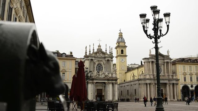 Turin, Piedmont, Italy. April 2019. A look at Piazza San Carlo. On the left in the foreground the fountain with the green bull, called turet, on the right the two twin churches. People are walking.