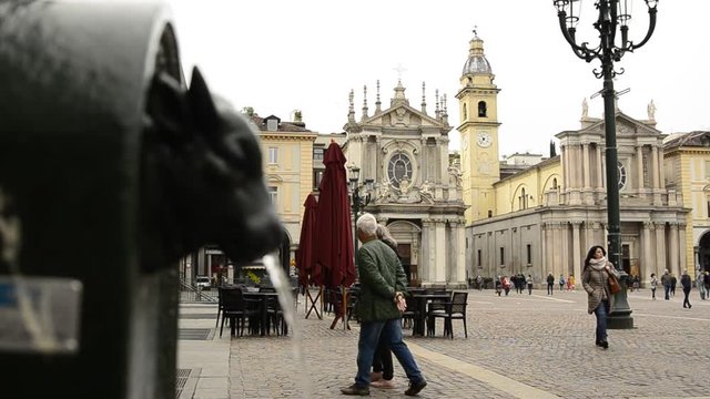 Turin, Piedmont, Italy. April 2019. A look at Piazza San Carlo. On the left in the foreground the fountain with the green bull, called turet, on the right the two twin churches. People are walking.