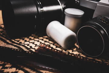 Old camera film and accessory with shemagh scarf on wooden table. travel equipment. copy space. retro style. closeup.
