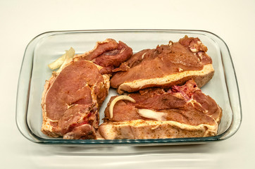 Large pieces of fresh pork fillet marinated and sprinkled with spices in a glassware for barbecue