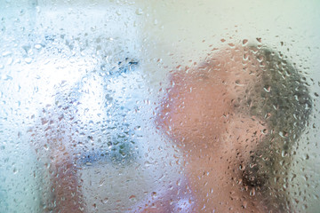 Fototapeta premium woman in the shower behind glass with drops