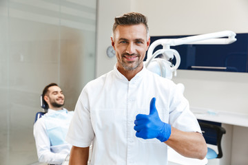 Handsome happy young man doctor in medical dentist center showing thumbs up.