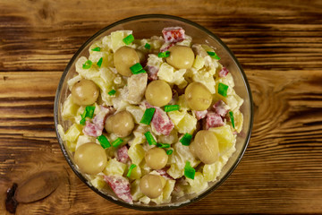 Potato salad with marinated mushrooms, sausage, onion and mayonnaise on wooden table
