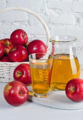 Apple juice in decanter and glass with apples close-up on white table.