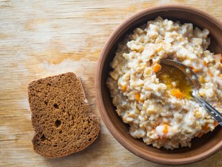 Bowl of oatmeal cooked with milk, pumpkin pieces and flavored with honey- slice of brown bread and spoon added