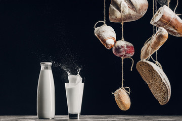 homemade bread hanging on ropes near splashing milk isolated on black with copy space