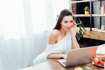 Attractive young woman using laptop at table in kitchen