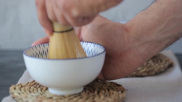 Man mixing green tea matcha in a bowl on blue surface. Drink is a rich source of antioxidants and polyphenols 