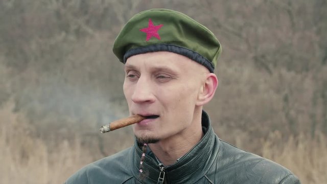 A man with a beard in a beret and a leather jacket smoking a cigar