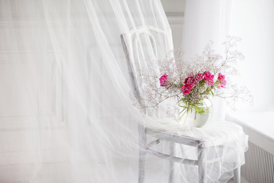 Still life with gipsofila and rose flowers in glass vase on retro chair